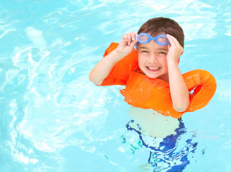 Young boy swimming in a life vest and taking pool safety precautions